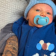 Rafaël a rejoint le concours — aidez-le/la à gagner de superbes lots ! baby, pacifier, hat, blue_outfit, tattooed_arm, bracelets, blanket, flower_tattoo, infant, cute, soft_texture, child, resting, knitted_hat, animal_print, cartoon_bear, balloons, clouds, person, portrait