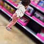 toddler, child, curly_hair, clothing, sweatshirt, pants, socks, store, aisle, shelf, valentines_day, cards, pink, box, floor, indoor, shopping, blurred_background, exploring, curious