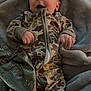 baby, infant, blanket, camo_onesie, clothing, cute, face, hand, lying_down, person, portrait, soft_texture, indoors, young_child, smiling, cozy, baby_garments, warm, child, comfort