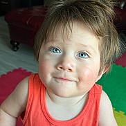 Marco is registered to the contest to win money with this photo: toddler, child, blue_eyes, orange_tank_top, dinosaur_print, indoor, colorful_mats, furniture, smile, hair, face, person, cute, young_child, portrait, playful, happy, casual_clothing, skin, head