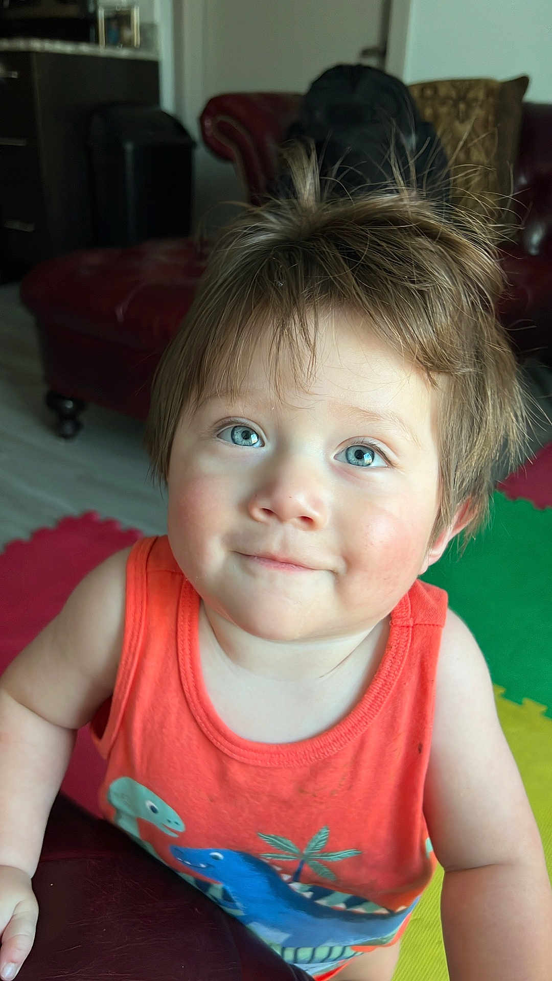 Marco is registered to the contest to win money with this photo: toddler, child, blue_eyes, orange_tank_top, dinosaur_print, indoor, colorful_mats, furniture, smile, hair, face, person, cute, young_child, portrait, playful, happy, casual_clothing, skin, head