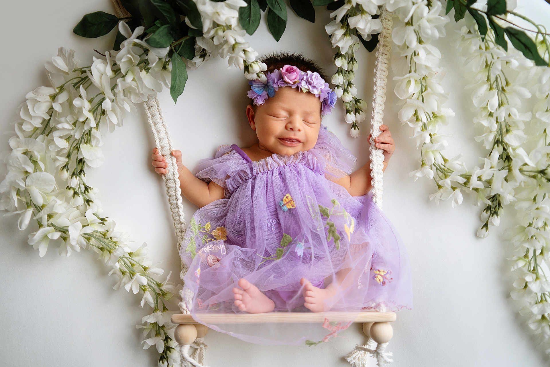 Hazeleigh is registered to the contest to win money with this photo: baby, newborn, infant, lavender_dress, floral_headband, swing, macrame, white_flowers, garland, tulle, smiling, eyes_closed, tiny_feet, hands, studio_shot, portrait, soft_lighting, peaceful, cute, decorative