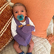 Elijah is registered to the contest to win money with this photo: baby, blue_socks, closeup, comfortable, cozy, cute, hedgehog_pattern, indoors, infant, lying_down, mittens, newborn, orange_pillows, pacifier, person, portrait, purple_knitted_outfit, quilted_blanket, soft_lighting, textured_pillows