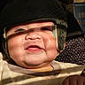 baby, child, infant, helmet, protective_gear, smiling, happy, portrait, close_up, face, eyes, mouth, indoor, sunlight, clothing, blanket, seated, photography, cozy, adorable