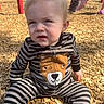 Owen Swartz is registered to the contest to win money with this photo: baby, child, toddler, playground, outdoor, sitting, portrait, face, expression, serious, striped_clothing, bear_costume, onesie, wood_chips, playground_equipment, sunlight, red_pole, park, blond_hair, close_up