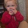 toddler, child, indoor, red_jacket, blonde_hair, blue_eyes, holding_object, curious, person, furniture, pillar, legs, cozy_clothing, portrait, young_child, looking_up, home, cute, casual, baby