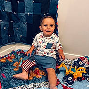 Isaiah joined the competition — help win amazing prizes! toddler, child, flag, american_flag, toy, excavator_toy, police_car_toy, quilt, patchwork, denim, blue_shorts, printed_shirt, indoor, corner, smiling, barefoot, happy, playtime, floor, casual_clothing