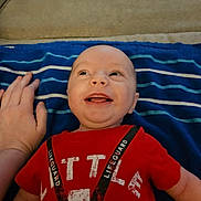 Maxwell joined the competition — help win amazing prizes! baby, blue_blanket, casual_clothing, child, cute, face, hand, happy, head, indoor, infant, lifeguard_text, lying_down, person, red_shirt, skin, smiling, striped_blanket, tongue_out, young_child