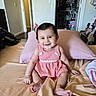 baby, child, smiling, pink_dress, bow, bed, pillow, indoor, person, happy, cute, hair, skin, furniture, room, blanket, sitting, foot, hand, face