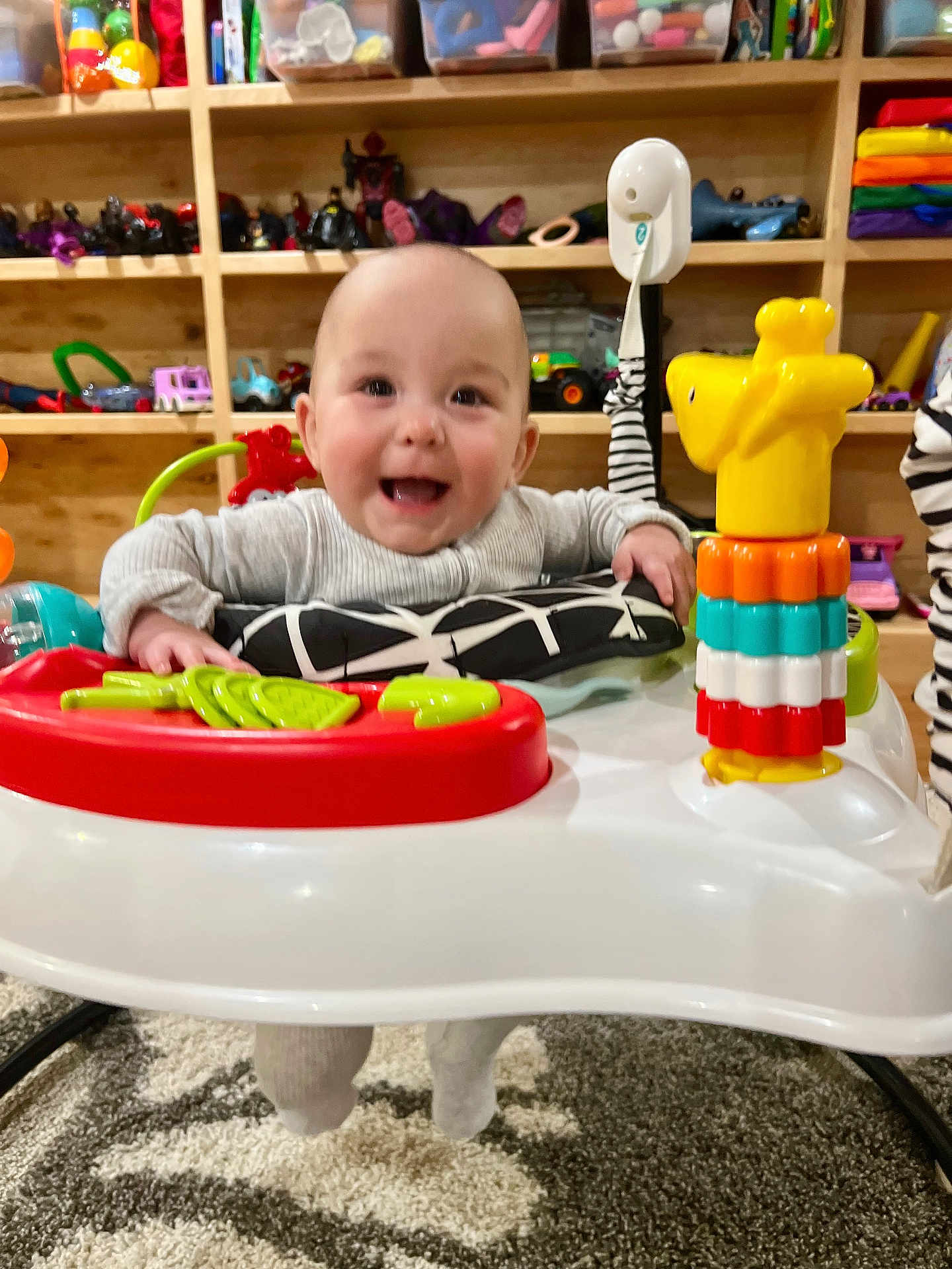 Brinley is registered to the contest to win money with this photo: baby, smiling, infant, baby_activity_center, toys, colorful, indoor, carpet, shelf, plastic_toys, child, playtime, happy, cute, person, young_child, room, furniture, background, face