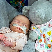 Brinley joined the competition — help win amazing prizes! baby, sleeping, nasal_cannula, infant, plush_toy, elephant, bib, onesie, hand, person, hospital, medical_tube, soft_toy, cute, peaceful, indoors, care, child, newborn, resting