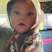 Rory is registered to the contest to win money with this photo: baby, child, hoodie, floral_pattern, indoor, portrait, face, eyes, curious, person, clothing, soft_lighting, expression, closeup, young_child, casual, warm, colorful_background, cute, infant