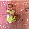 baby, infant, smiling, pink_blanket, milestone_blanket, stars, numbers, yellow_clothing, cute, happy, lying_down, portrait, child, feet, hands, headband, face, months, heart_marker, indoor