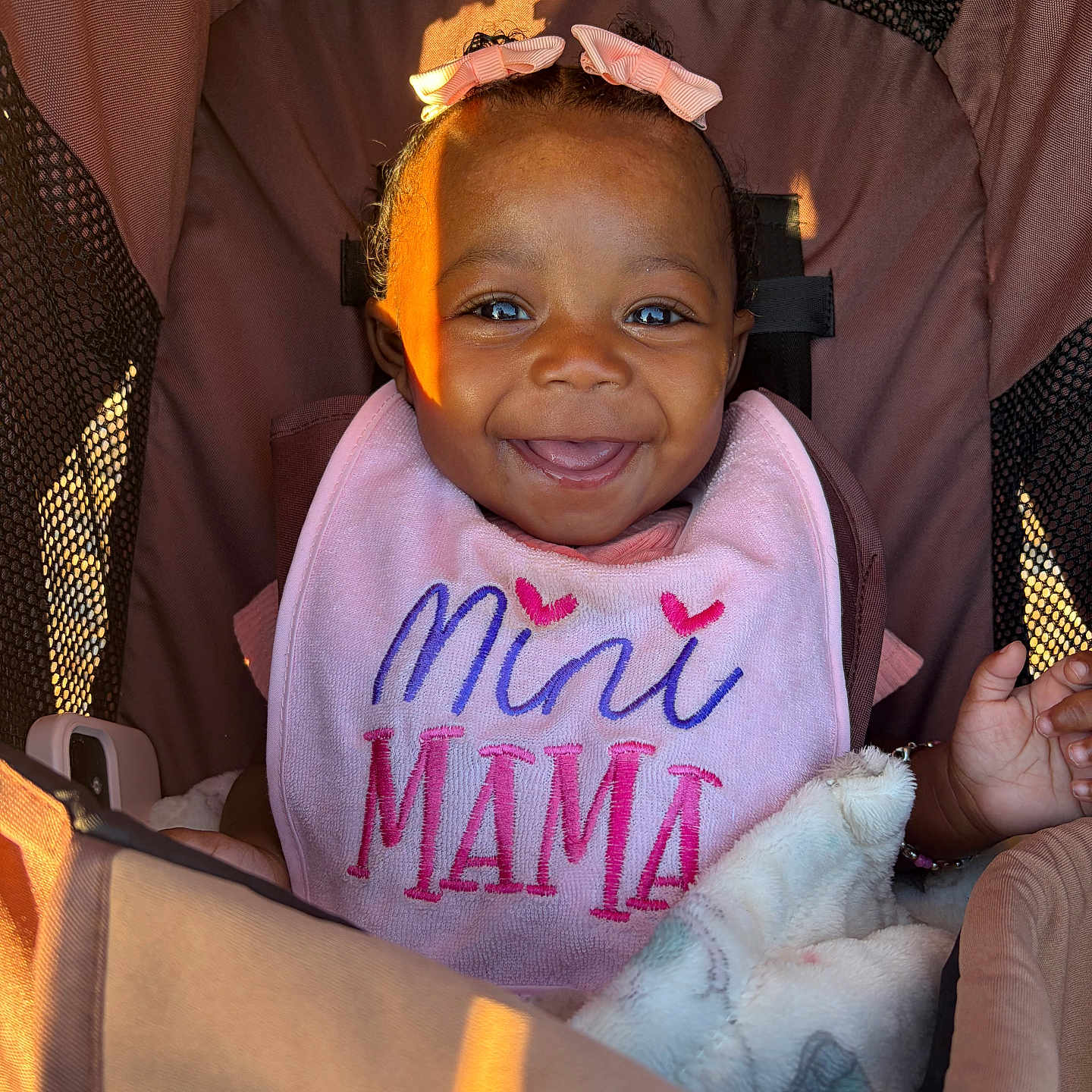 Azani joined the competition — help win amazing prizes! baby, baby_girl, blanket, bows, child, closeup, clothing, cute, face, hands, happy, infant, person, pink_bib, portrait, seated, smiling, stroller, sunlight, young_child
