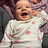 Winter is registered to the contest to win money with this photo: baby, infant, child, smiling, laughing, portrait, indoors, blanket, purple_blanket, onesie, clothing, sun_pattern, face, eyes, mouth, adult_hand, sitting, cozy, happy, close_up