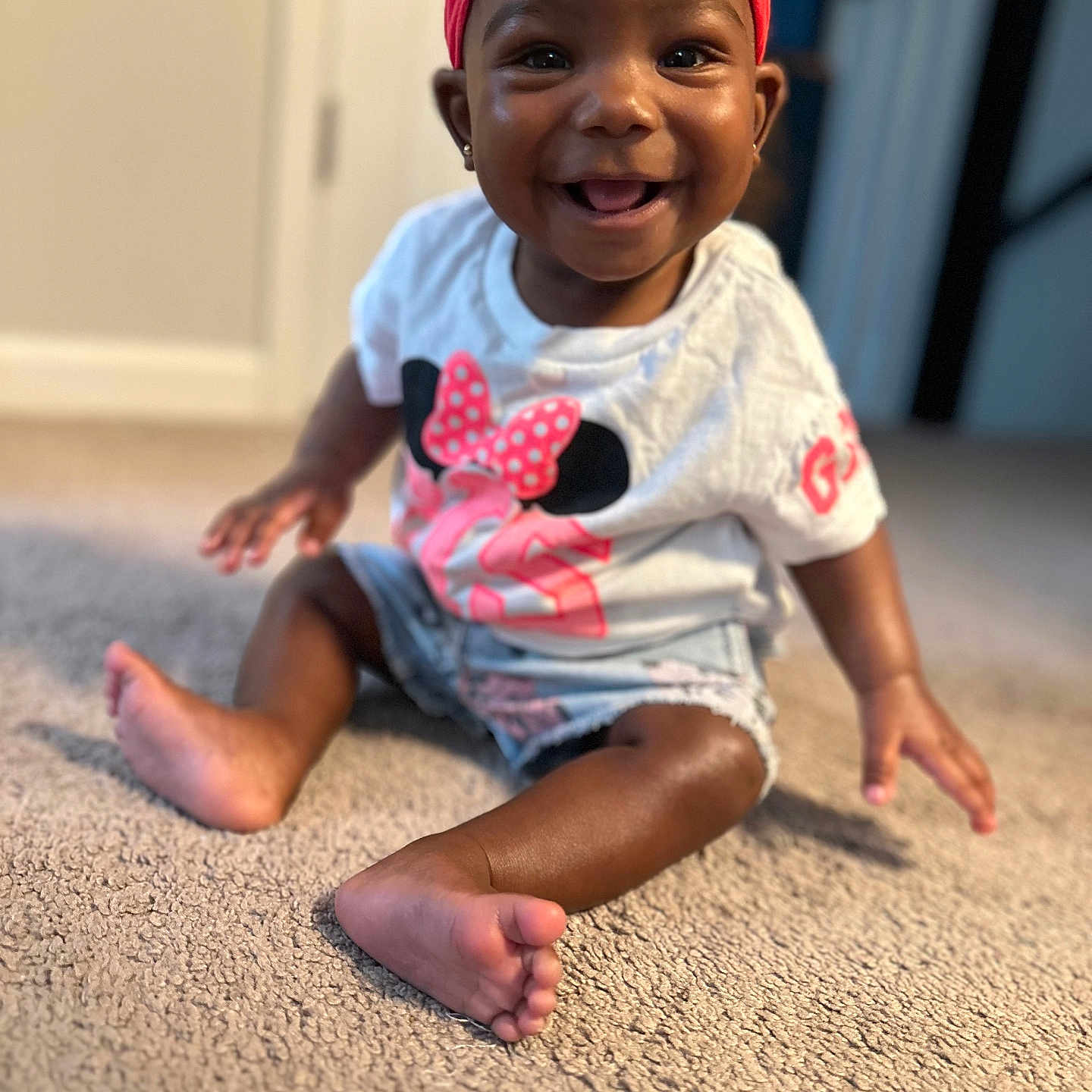 Giana is registered to the contest to win money with this photo: baby, bow, carpet, child, clothing, cute, face, foot, hand, happy, headband, indoor, infant, person, pink, portrait, shorts, sitting, smiling, tshirt