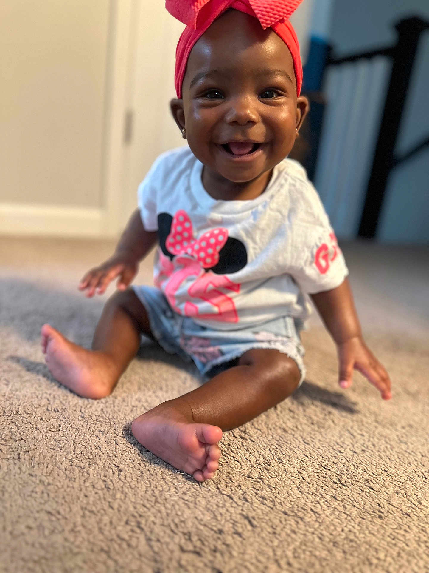 Giana is registered to the contest to win money with this photo: baby, bow, carpet, child, clothing, cute, face, foot, hand, happy, headband, indoor, infant, person, pink, portrait, shorts, sitting, smiling, tshirt