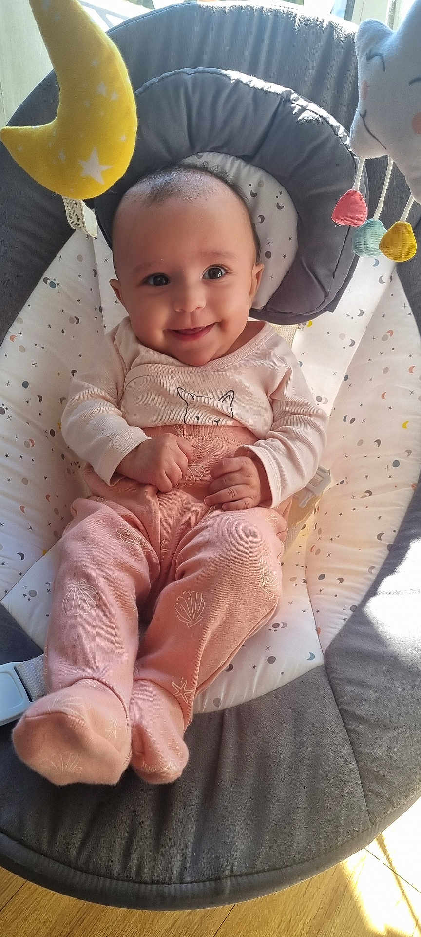 Louana a rejoint le concours — aidez-le/la à gagner de superbes lots ! baby, baby_seat, child, cushion, cute, face, footed_pants, happy, indoor, infant, long_sleeve, moon_toy, person, pink_clothing, relaxing, smile, star_toy, sunlight, toy, wooden_floor