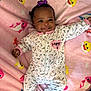 baby, child, smile, onesie, blanket, pink, purple_bow, milk_bottle_pattern, happy_text, lying_down, cute, infant, face, clothing, pattern, soft_texture, colorful, indoor, portrait, joyful