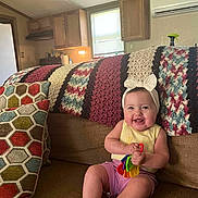 Raelynn is registered to the contest to win money with this photo: baby, child, smiling, headband, toy, couch, blanket, pillow, crochet, home, indoor, child_playing, happy, seated, furniture, colorful, person, infant, cute, living_room