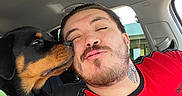 Xeniah is registered to the contest to win money with this photo: dog, puppy, rottweiler, man, face, licking, car, interior, casual, tattoo, red_shirt, seat, window, daylight, happy, affection, closeup, pet, smile, friendship