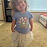 child, girl, toddler, smiling, curly_hair, portrait, standing, indoor, home, living_room, sunlight, window, blinds, carpet, skirt, polka_dots, floral_shirt, sandals, fashion, happy