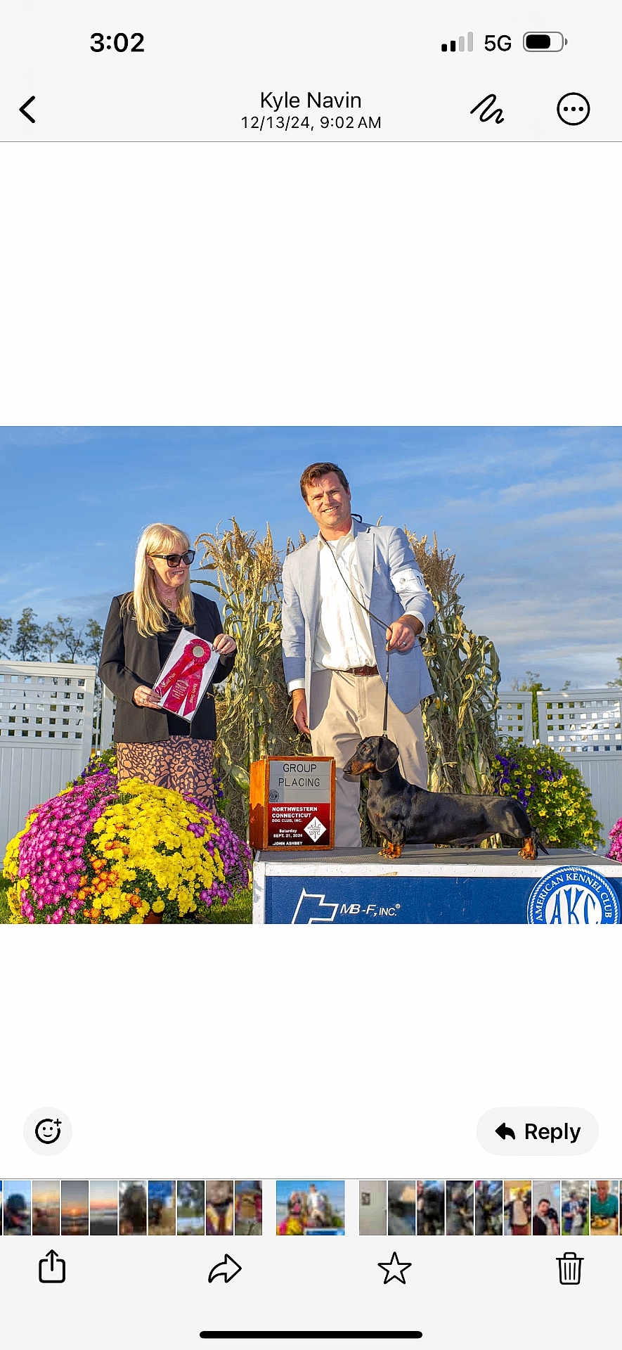 Sebastian is registered to the contest to win money with this photo: dog, dachshund, award, ribbon, podium, american_kennel_club, person, man, woman, flowers, cornstalks, outdoor, sunny, smiling, blue_sky, event, competition, proud, leash, clothing