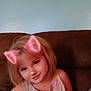child, girl, smile, face_filter, cat_ears, pink, couch, indoor, blonde_hair, tank_top, portrait, happy, young, wall_art, home, casual, cute, person, sitting, digital_filter