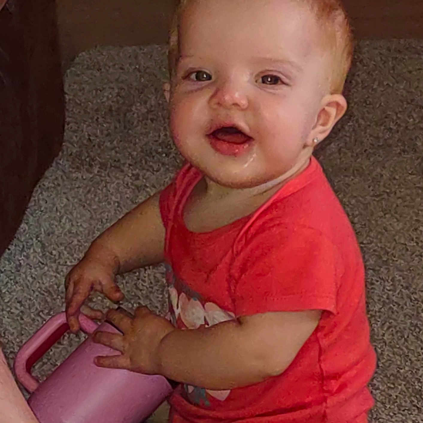 Lilliana is registered to the contest to win money with this photo: baby, carpet, child, curious, cute, earring, floor, hand, indoor, messy_face, person, pink_cup, red_hair, red_shirt, short_sleeve, sitting, skin, smiling, toddler, young_child