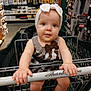 Lilliana is registered to the contest to win money with this photo: baby, shopping_cart, headband, bow, dress, hardware_store, tools, shelves, store_aisle, child, infant, shopping, grip, happy, cute, retail, retail_environment, person, indoor, foot