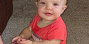 Lilliana is registered to the contest to win money with this photo: baby, child, red_hair, carpet, indoor, sitting, smiling, sippy_cup, red_shirt, cute, person, floor, young_child, infant, holding, playful, happy, light_skin, short_hair, casual_clothing