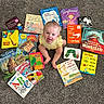baby, child, infant, sitting, smiling, open_mouth, portrait, books, childrens_books, storybook, reading, carpet, indoor, colorful, yellow_clothing, overhead_view, playful, happy, education, book_collection