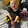 baby, child, infant, smiling, happy, portrait, indoor, bedroom, bed, bedding, clothing, laundry, yellow_bow, headband, sunflower, black_outfit, hairbrush, sitting, patterned_blanket, close_up