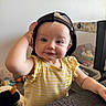 Bexley is registered to the contest to win money with this photo: baby, child, infant, portrait, smiling, face, blue_eyes, blonde_hair, backward_cap, yellow_outfit, striped_clothing, sleeveless_dress, sitting, standing, indoor, home, playroom, toys, playpen, furniture