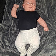 Bruce joined the competition — help win amazing prizes! baby, infant, black_shirt, light_pants, cloud_patch, blanket, gray_blanket, soft_texture, lying_down, raised_arm, fist, cute, indoors, portrait, child, newborn, clothing, person, baby_clothes, expression