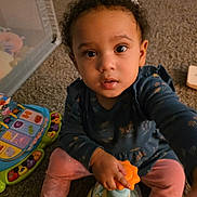 Elara is registered to the contest to win money with this photo: toddler, child, toy, carpet, indoor, curly_hair, pink_pants, blue_shirt, hand, face, eyes, play, floor, baby, cute, infant, person, childhood, expression, home