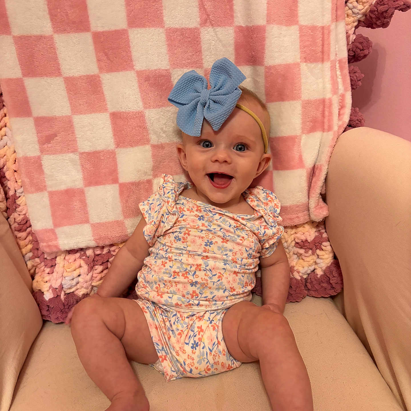 Cassidy joined the competition — help win amazing prizes! baby, child, smile, blue_bow, floral_outfit, blanket, checkered_pattern, pink, beige_chair, happy, cute, indoor, infant, headband, seated, legs, arms, face, portrait, cozy