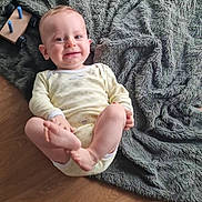 Gabriel a rejoint le concours — aidez-le/la à gagner de superbes lots ! baby, blanket, candid, child, cozy, cute, face, feet, floor, hand, happy, indoor, infant, onesie, person, playful, smile, texture, toy, wooden_floor