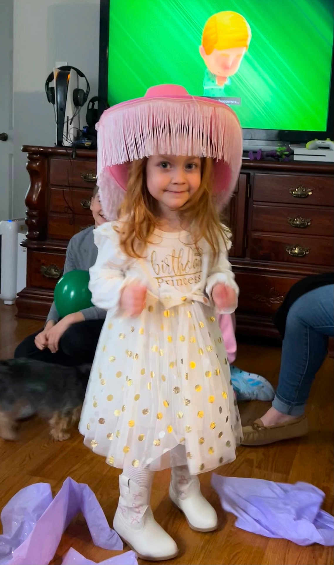 Emily joined the competition — help win amazing prizes! child, birthday, princess, hat, pink, dress, gold_polka_dots, boots, living_room, balloon, dog, wooden_floor, tissue_paper, television, furniture, smile, celebration, person, indoor, happy