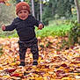 child, toddler, autumn, leaves, fall, outdoor, nature, forest, hat, camo_pants, smiling, happy, walking, seasonal, young_child, clothing, greenery, daylight, playful, exploring