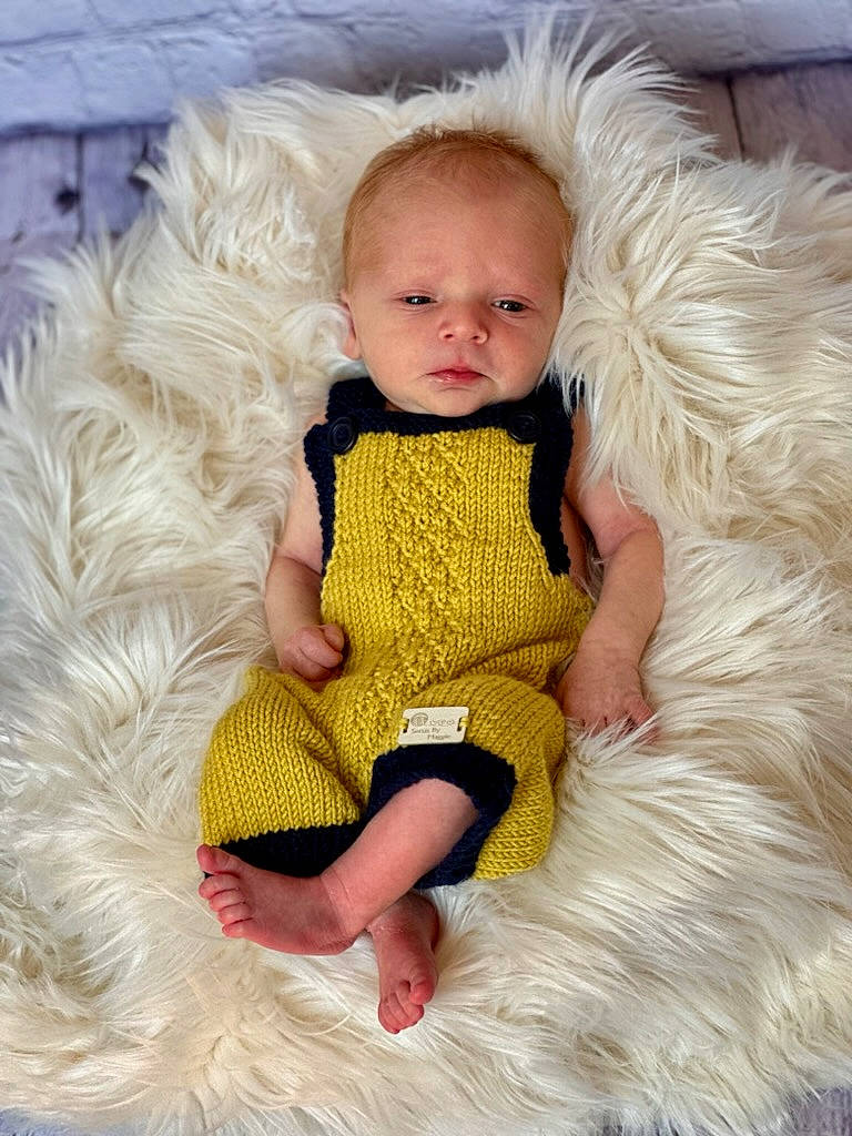 baby, child, cozy, cute, face, fluffy_rug, hands, indoor, infant, knitted_outfit, newborn, person, portrait, relaxed, resting, sleepy_eyes, small_feet, soft_texture, warm, yellow_clothing