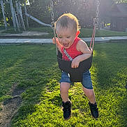 Jackson joined the competition — help win amazing prizes! toddler, child, swing, playground, grass, sunlight, happy, smiling, outdoor, summer, casual_clothing, black_shoes, red_tank_top, denim_shorts, park, play_equipment, joyful, fun, daylight, nature