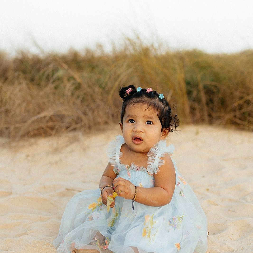 Aria joined the competition — help win amazing prizes! baby, barefoot, beach, bracelets, candid, child, curious_expression, cute, dress, dunes, floral_dress, grass, hair_bows, hands, outdoor, portrait, sand, sitting, sunshine, toddler