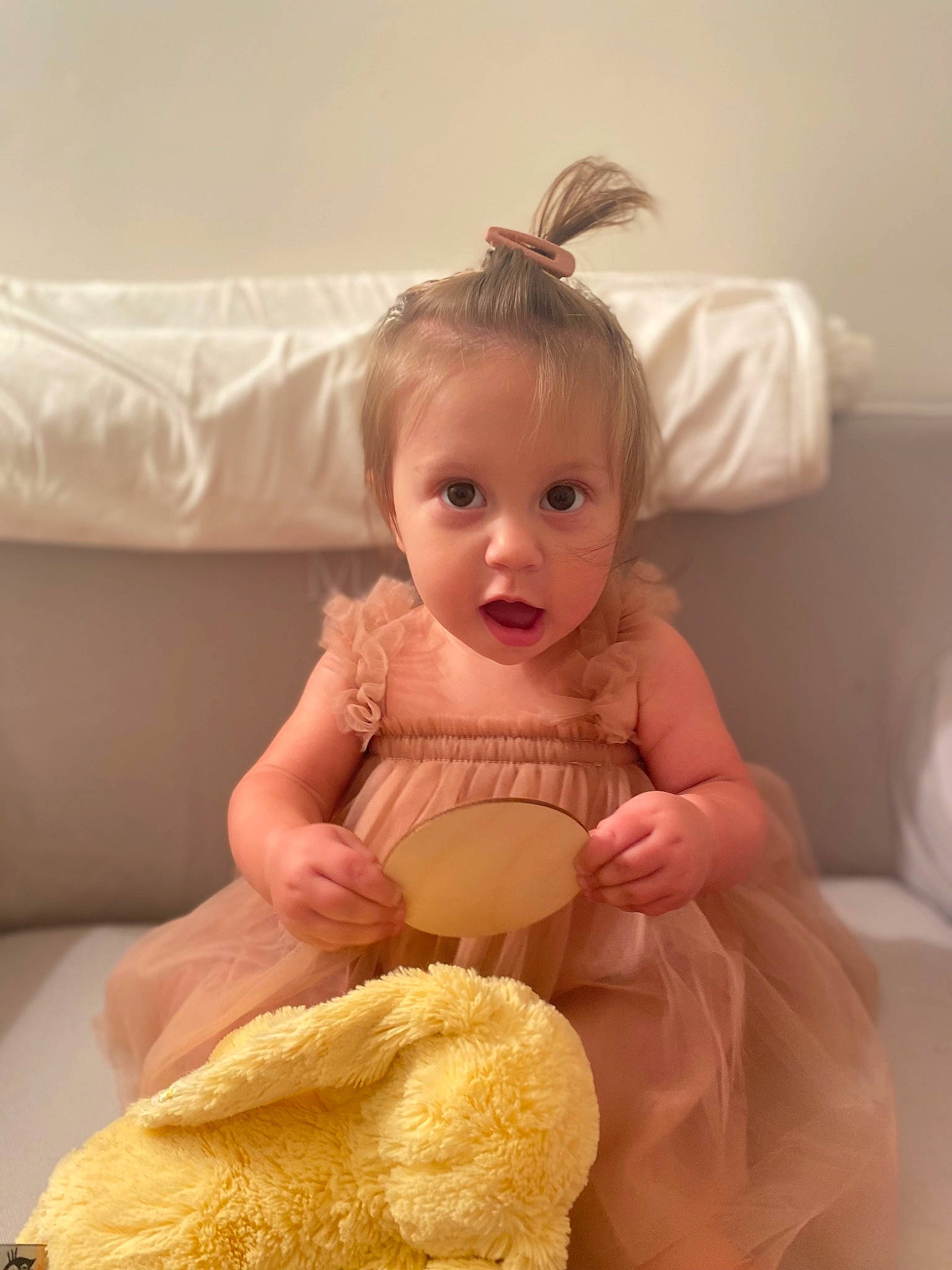 Marin is registered to the contest to win money with this photo: abdomen, arm, baby, baby_toddler_clothing, blond, child, comfort, facial_expression, happy, headpiece, human_leg, linens, peach, person, room, ruffle, sitting, skin, surprise, sweetness