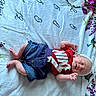 baby, infant, child, smiling, clothing, red_shirt, denim_shorts, headband, blanket, floral_pattern, bottle, sleeping, happy, cute, lying_down, indoors, person, baby_bottle, fabric, soft_texture