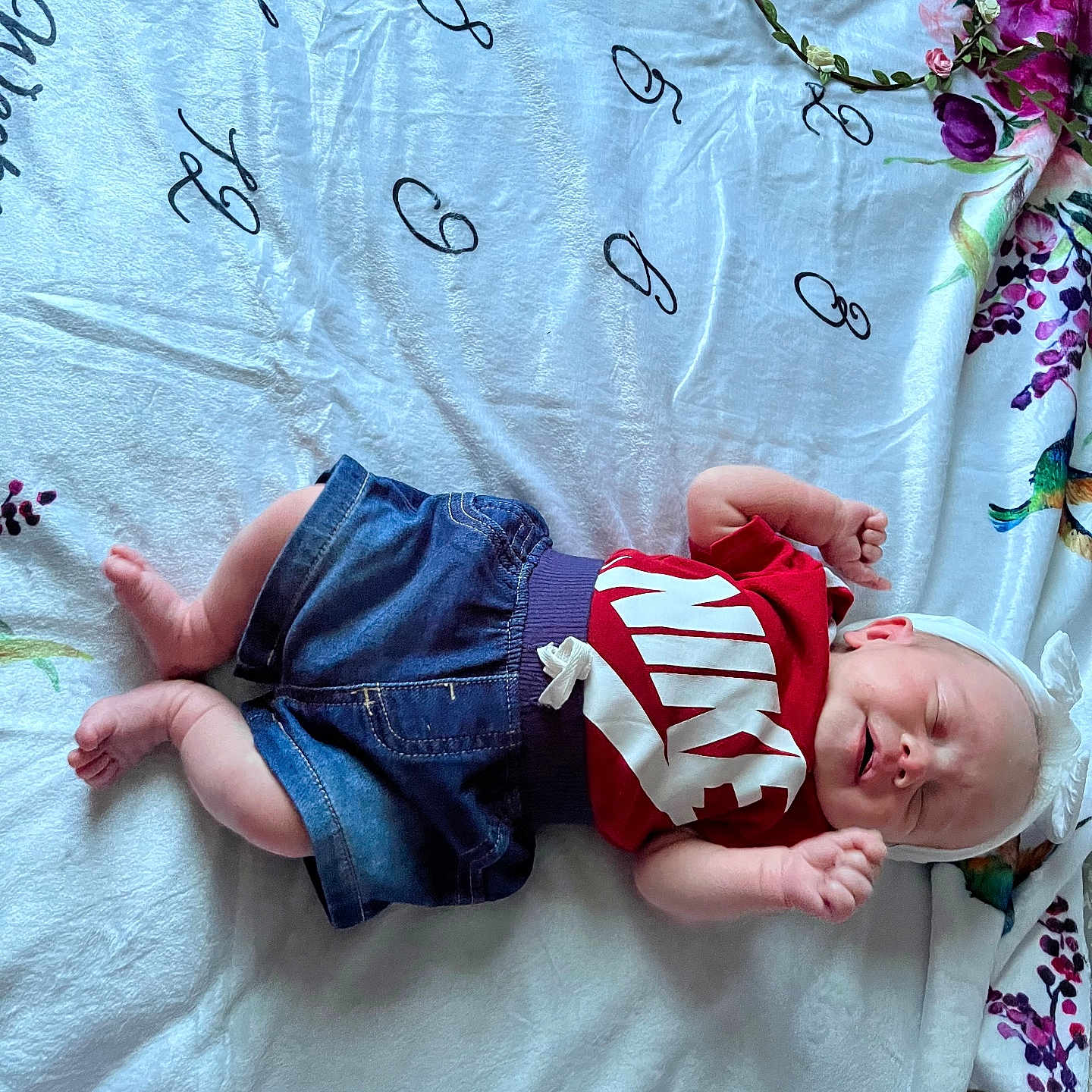 Bailee is registered to the contest to win money with this photo: baby, infant, child, smiling, clothing, red_shirt, denim_shorts, headband, blanket, floral_pattern, bottle, sleeping, happy, cute, lying_down, indoors, person, baby_bottle, fabric, soft_texture