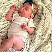 Emery is registered to the contest to win money with this photo: baby, newborn, sleeping, onesie, headband, blue_bow, blanket, knitted_blanket, cozy, infant, peaceful, cute, soft, portrait, indoor, person, skin, hand, leg, closeup