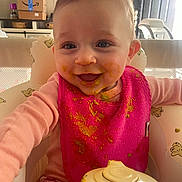 Kasey is registered to the contest to win money with this photo: baby, infant, toddler, highchair, bib, bib_stained, baby_food, messy, smile, face, eyes, clothing, pink, feeding_bottle, food_container, indoor, living_room, television, door, happy