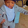 child, toddler, portrait, standing, indoors, beanie, heart, tracksuit, hoodie, sneakers, gray_clothing, fashion, streetwear, looking_down, serious_expression, carpet, chair, toys, living_room, full_body
