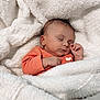 baby, sleeping, blanket, orange_clothing, infant, cozy, soft_texture, peaceful, cute, newborn, wrapped, hand, face, portrait, resting, indoor, warm, comfort, closeup, child